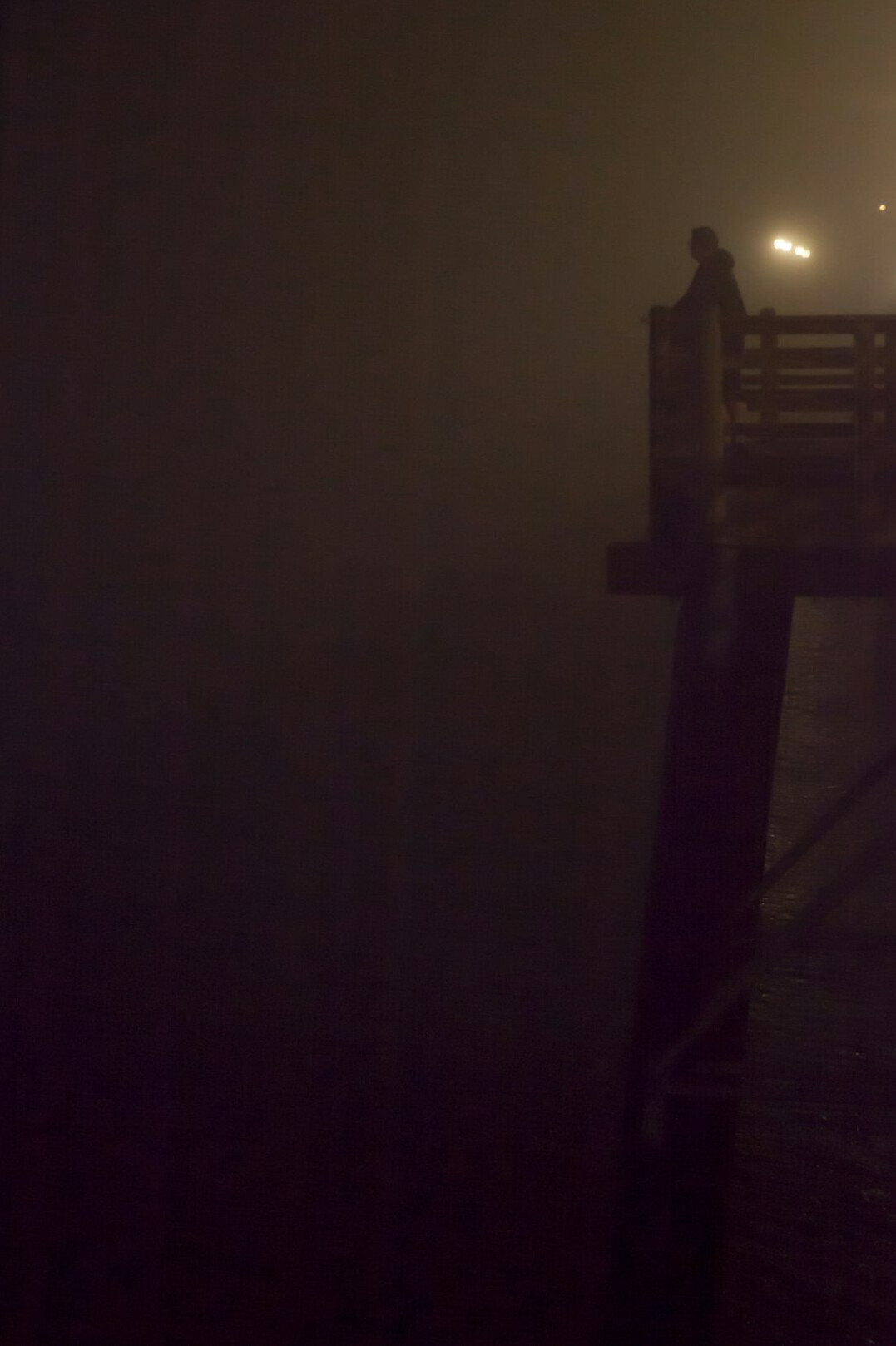 Moody photo of a foggy pier at night with a single lit lamppost